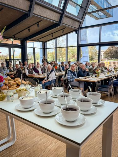 Der Tee steht bereit: gedeckter Tisch mit Tassen vor den voll besetzten Tischreihen der Krantine