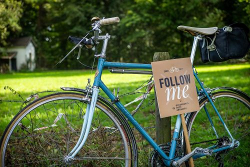 „Follow me“-Wegweiser lehnt am blauen Vintage-Rennrad