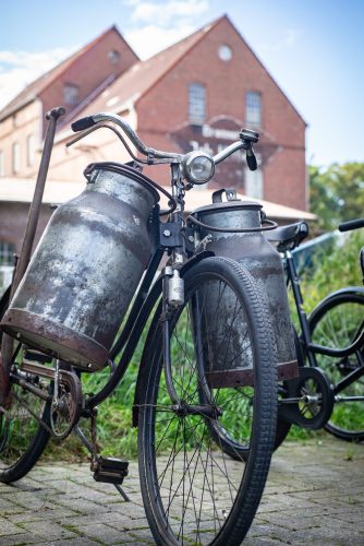 Nostalgie pur: Oldtimer-Fahrrad mit zwei Milchkannen am Lenker vor historischem Backstein