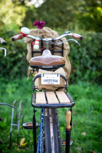 Ledersattel, Gepäckträger und Tweed-Run-Starternummer: ein Vintage-Rad von hinten vor grüner Hecke